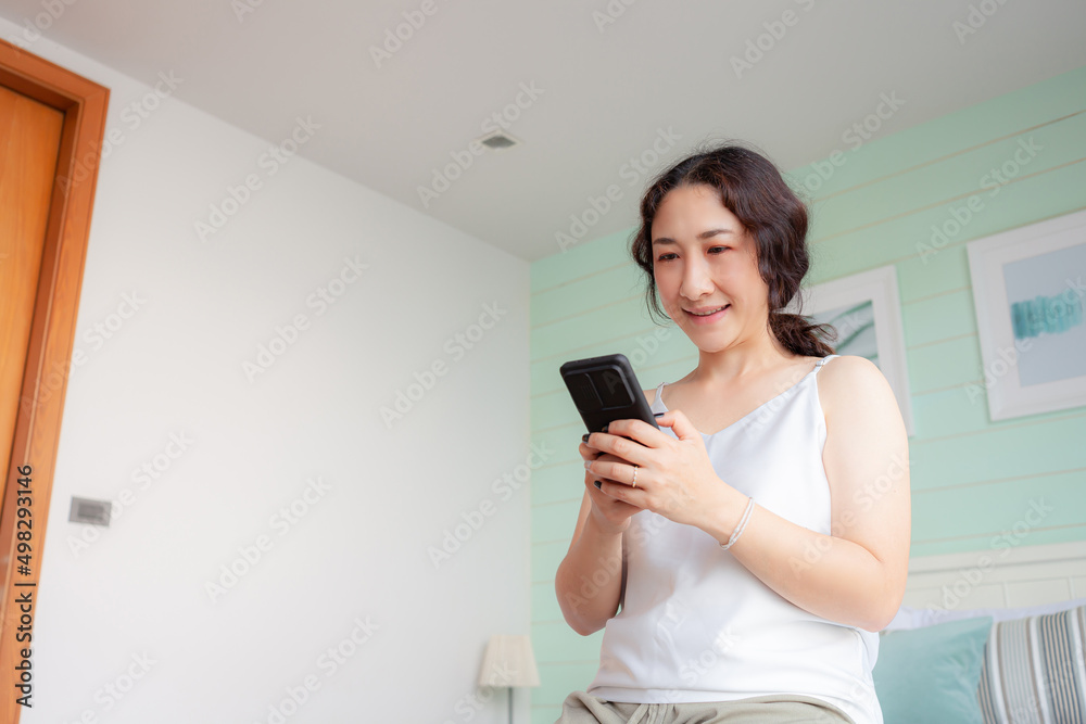 Happy asian woman using mobile phone at home. Asian housewife checking social media holding with smartphone. relax woman using mobile phone app playing ordering delivery, shopping online, video call Happy asian woman using mobile phone at home. Asian housewife checking social media holding with smartphone. relax woman using mobile phone app playing ordering delivery, shopping online, video call