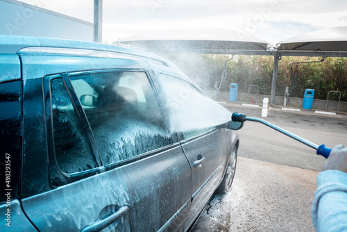 Lavagem de carro com bomba de equipamento de água de alta pressão no auto atendimento ao ar livre. Veículo coberto com detergentes químicos  photo