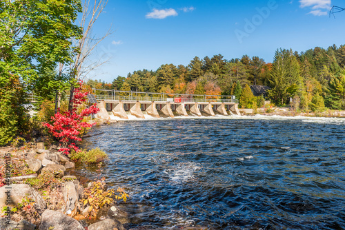 View of a small dam on a river with wooded banks on a sunny autumn day