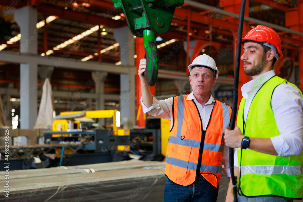 Engineering factory worker control indoor overhead crane to lift up metal construction object on metal sheet factory. Engineering factory worker control indoor overhead crane to lift up metal construction object on metal sheet factory.