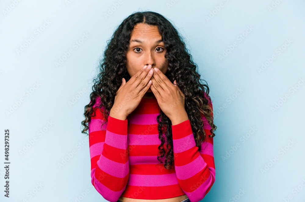 Young hispanic woman isolated on blue background covering mouth with hands looking worried. Young hispanic woman isolated on blue background covering mouth with hands looking worried.