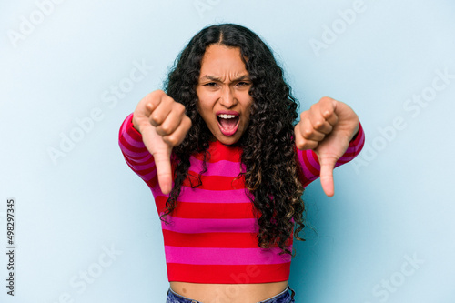 Young hispanic woman isolated on blue background showing thumb down and expressing dislike. © Asier