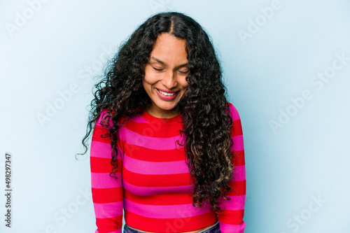 Young hispanic woman isolated on blue background laughs and closes eyes, feels relaxed and happy. © Asier