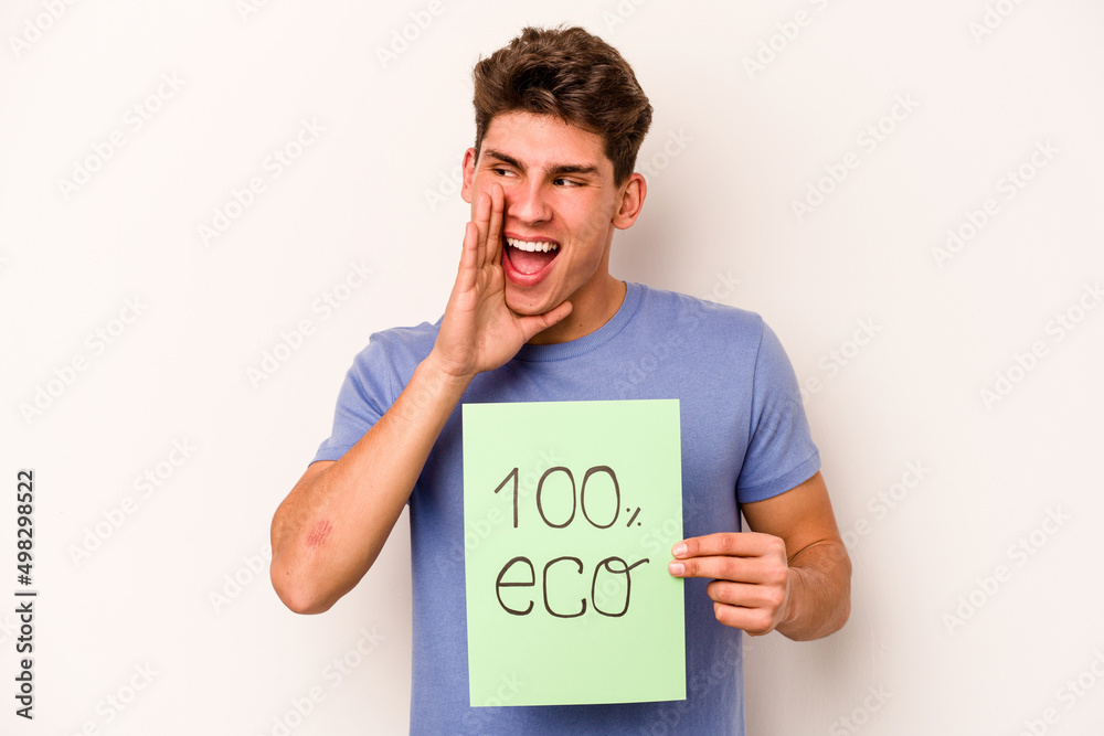 Young caucasian man holding 100% eco placard isolated on white background shouting and holding palm near opened mouth. Young caucasian man holding 100% eco placard isolated on white background shouting and holding palm near opened mouth.