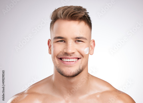 It works like a dream. Studio shot of a young man applying moisturizer to his face against a grey background.
