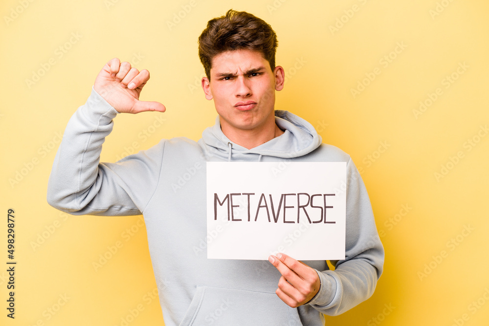 Young caucasian man holding metaverse placard isolated on yellow background feels proud and self confident, example to follow. Young caucasian man holding metaverse placard isolated on yellow background feels proud and self confident, example to follow.