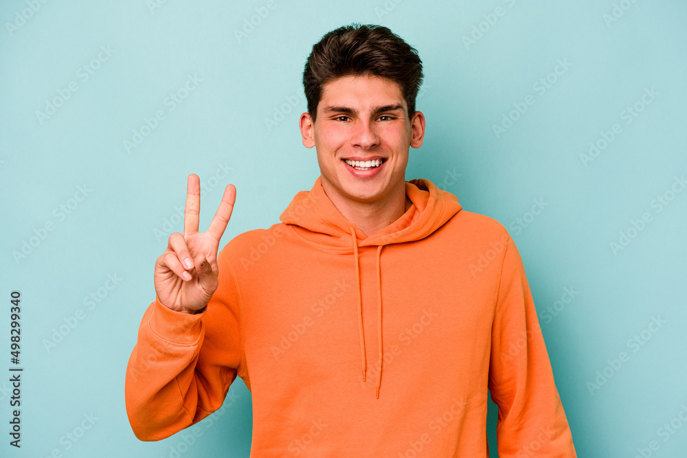 Young caucasian man isolated on blue background showing victory sign and smiling broadly. Young caucasian man isolated on blue background showing victory sign and smiling broadly.