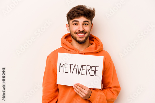 Young hispanic man holding a metaverse placard isolated on white background happy, smiling and cheerful.