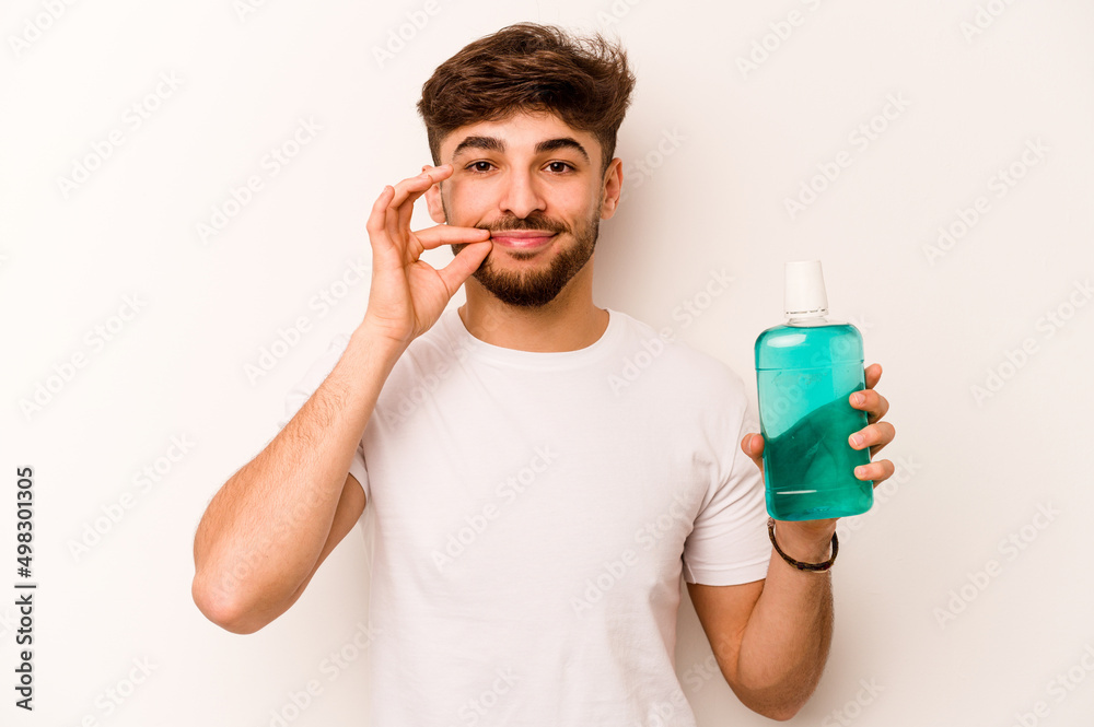 Young hispanic man holding mouthwash isolated on white background with fingers on lips keeping a secret. Young hispanic man holding mouthwash isolated on white background with fingers on lips keeping a secret.
