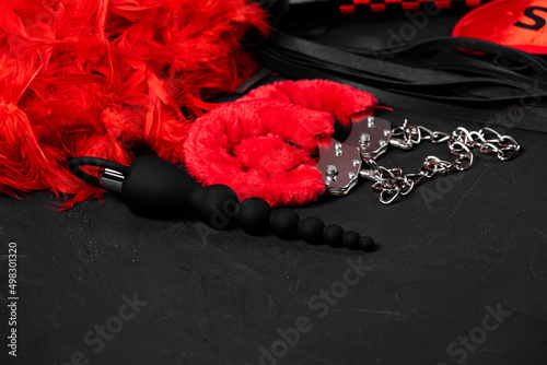 BDSM, bondage play, fetish wear and kinky sex toy concept with close up on erotic mask and red handcuffs isolated on black silk background