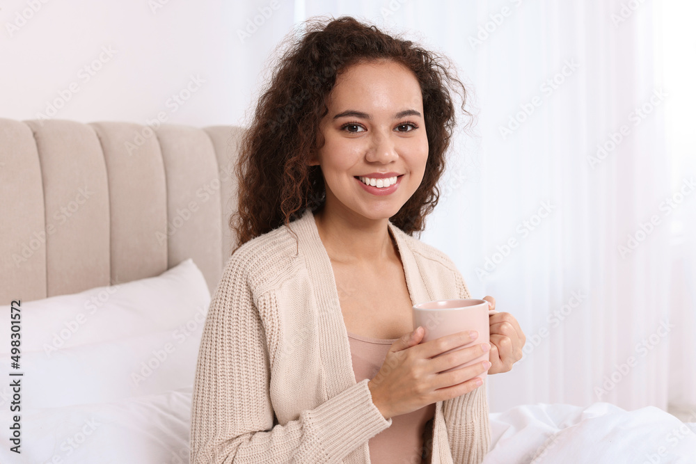 Happy African American woman with cup of drink in bed at home Happy African American woman with cup of drink in bed at home