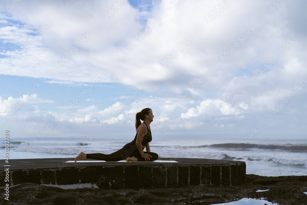 Young woman practice yoga on a beautiful beach at sunrise. Blue sky, ocean, waves, proximity to nature, unity with nature.