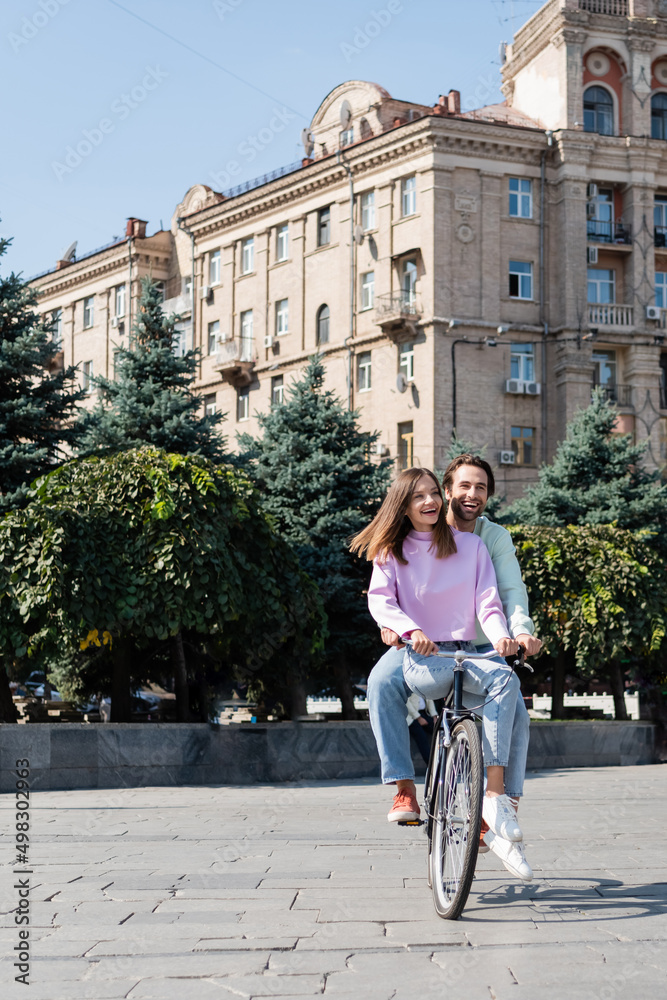 Cheerful young couple riding bicycle on urban street.