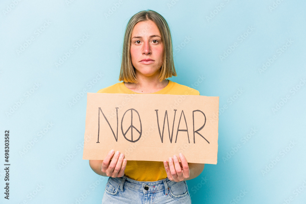 Young caucasian woman holding no war placard isolated on blue background Young caucasian woman holding no war placard isolated on blue background