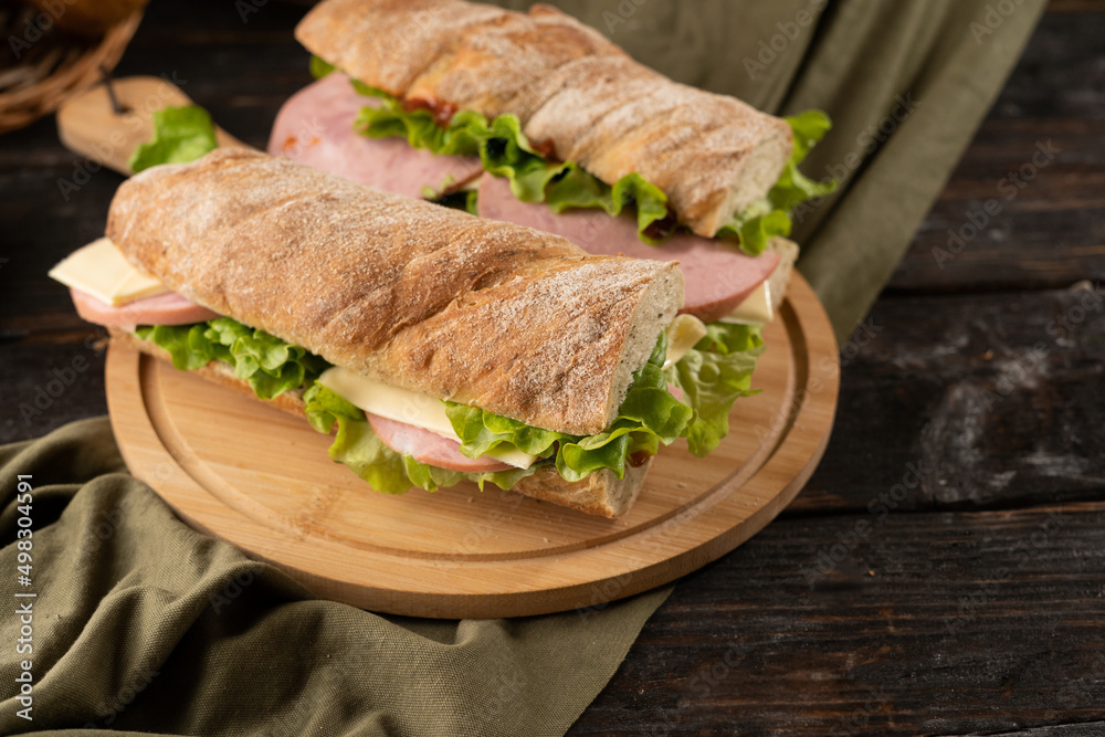 Two fresh sandwiches with ham, cheese, lettuce, on a wooden cutting board.