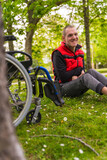 Portrait of a person with a disability sitting on the grass next to a wheelchair next to a tree laughing out loud