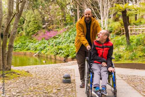 a person with a disability in a wheelchair being pushed by a friend in a public city park photo