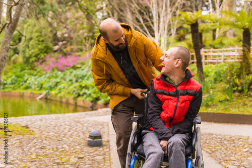a person with a disability in the wheelchair being pushed by a friend in a public city park, having fun in spring