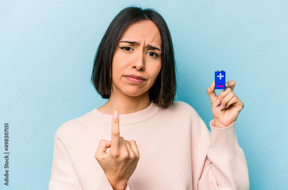 Young hispanic woman holding batteries isolated on blue background pointing with finger at you as if inviting come closer. Young hispanic woman holding batteries isolated on blue background pointing with finger at you as if inviting come closer.