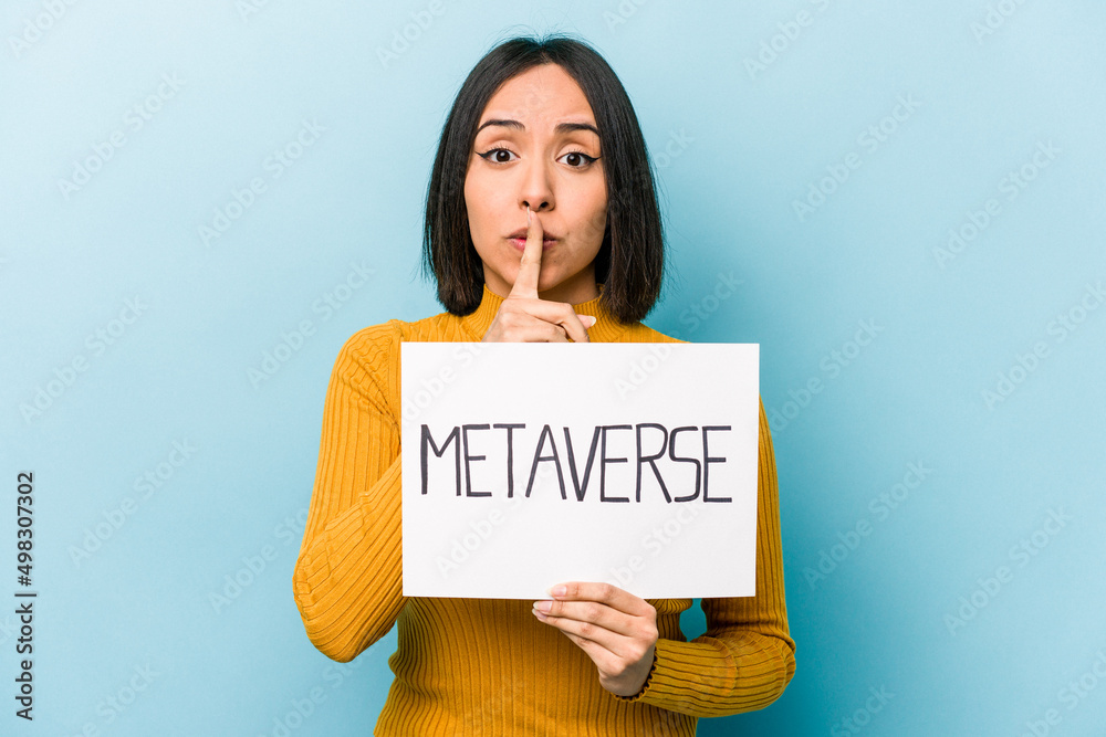 Young hispanic woman holding metaverse placard isolated on blue background keeping a secret or asking for silence. Young hispanic woman holding metaverse placard isolated on blue background keeping a secret or asking for silence.