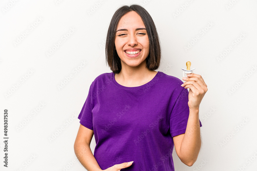 Young hispanic pregnant woman holding pacifier isolated on white background laughing and having fun. Young hispanic pregnant woman holding pacifier isolated on white background laughing and having fun.