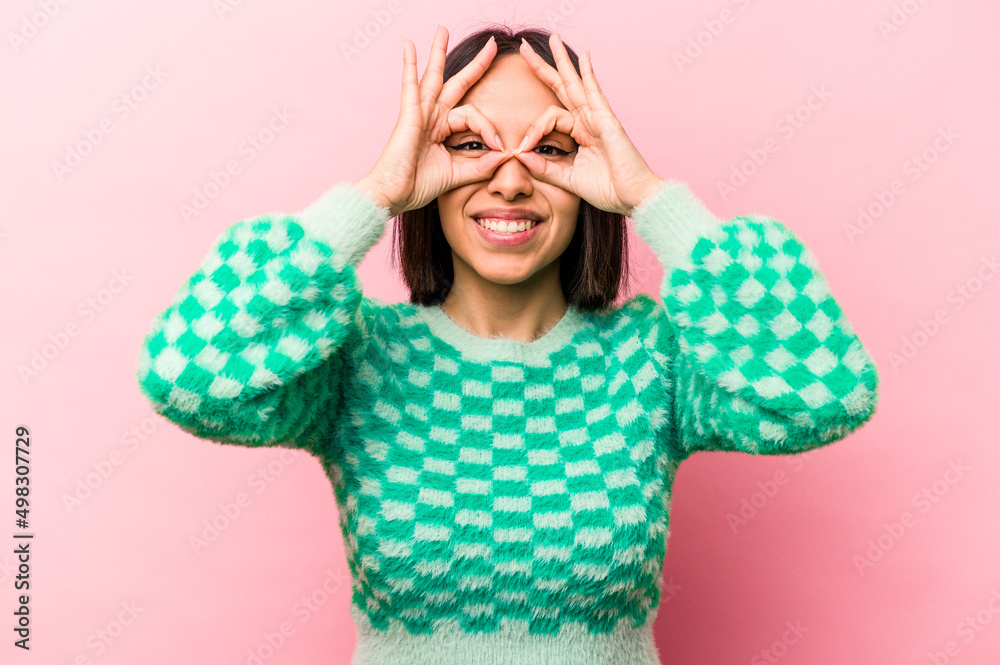 Young hispanic woman isolated on pink background showing okay sign over eyes Young hispanic woman isolated on pink background showing okay sign over eyes