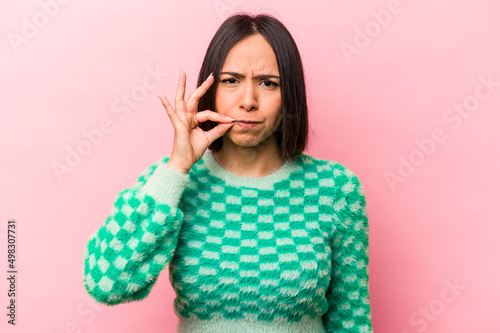 Young hispanic woman isolated on pink background with fingers on lips keeping a secret.