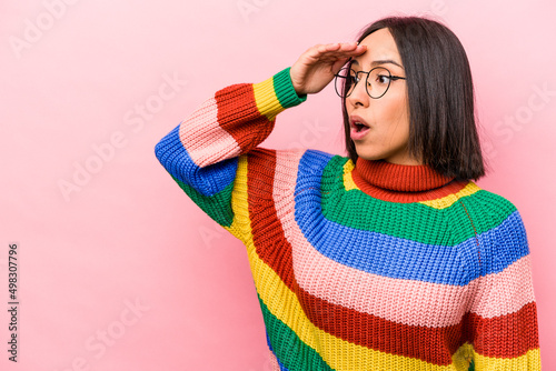 Young hispanic woman isolated on pink background looking far away keeping hand on forehead.