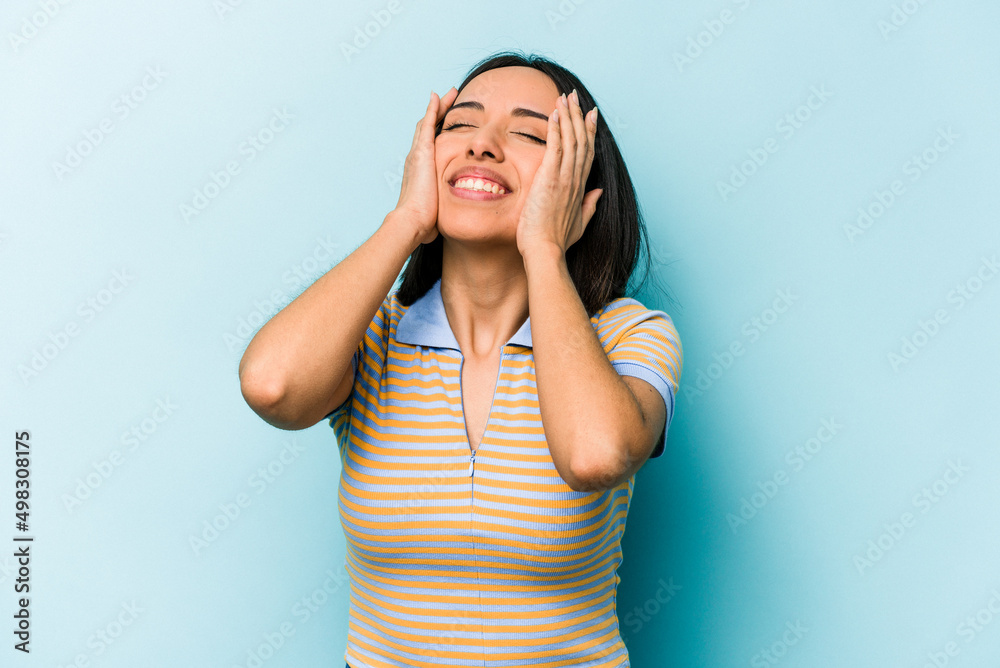 Young hispanic woman isolated on blue background laughs joyfully keeping hands on head. Happiness concept. Young hispanic woman isolated on blue background laughs joyfully keeping hands on head. Happiness concept.