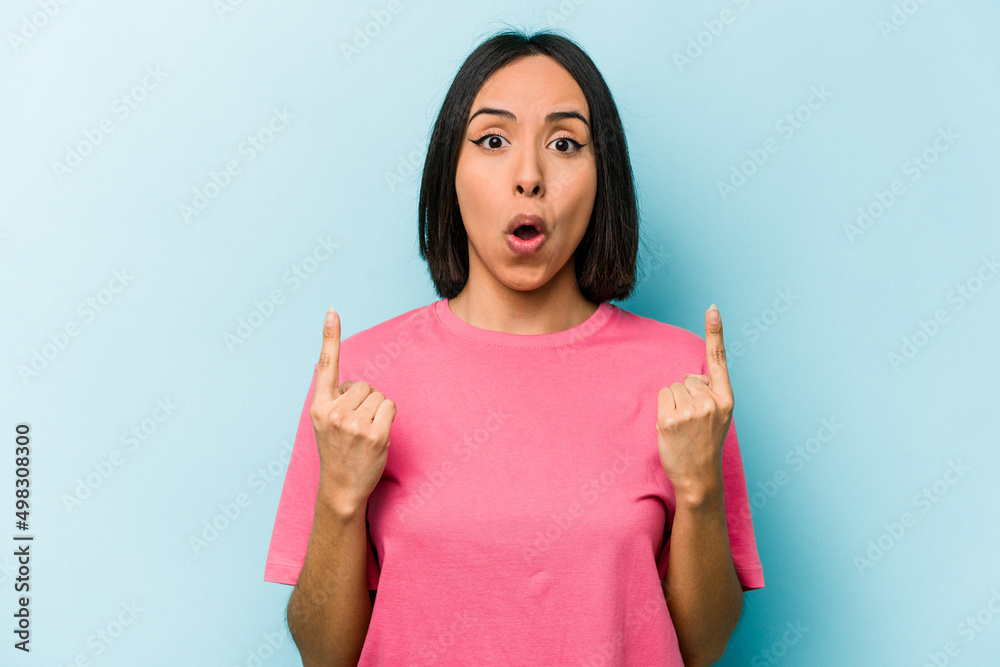 Young hispanic woman isolated on blue background pointing upside with opened mouth. Young hispanic woman isolated on blue background pointing upside with opened mouth.