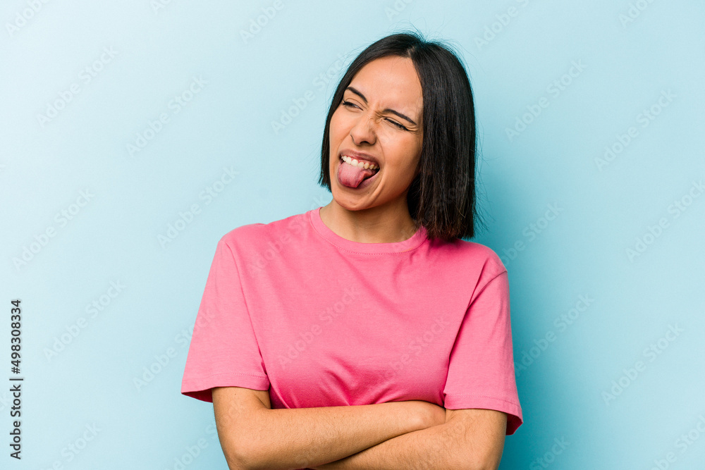 Obraz premium Young hispanic woman isolated on blue background funny and friendly sticking out tongue.