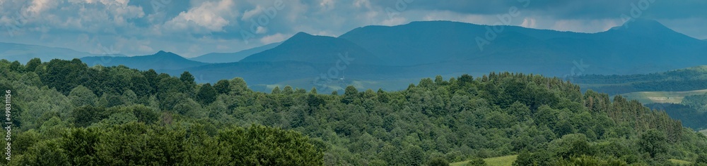 Panoramic green forest on blue mountains and sky background. View of the Carpathian mountains in spring, Ukraine. Mountain tourism. Tourism and travel concept.