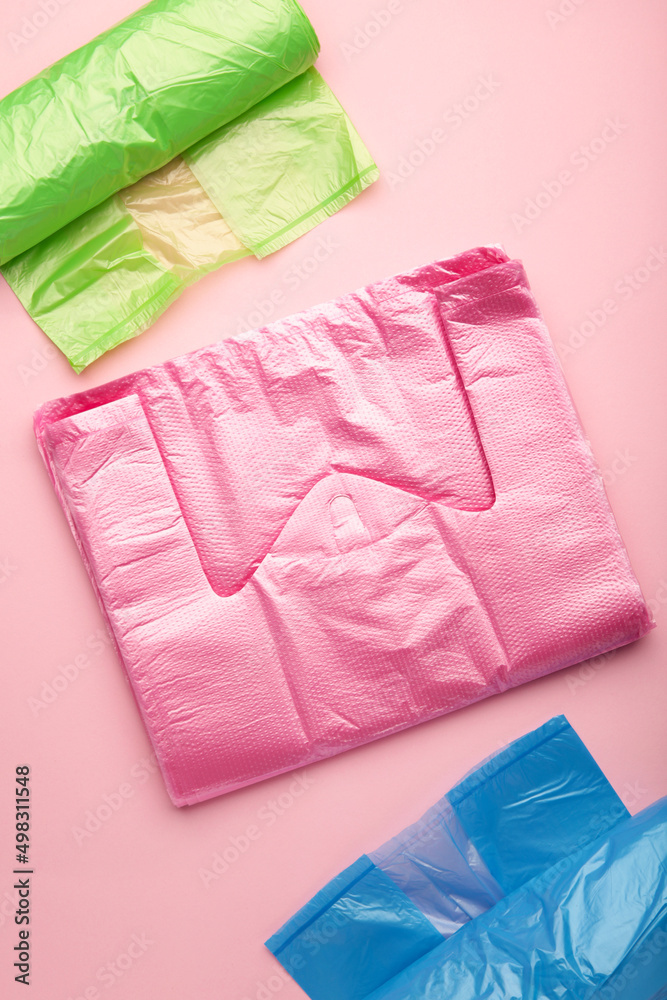 A lot of colored plastic bags rolls on a pink background. Vertical photo.