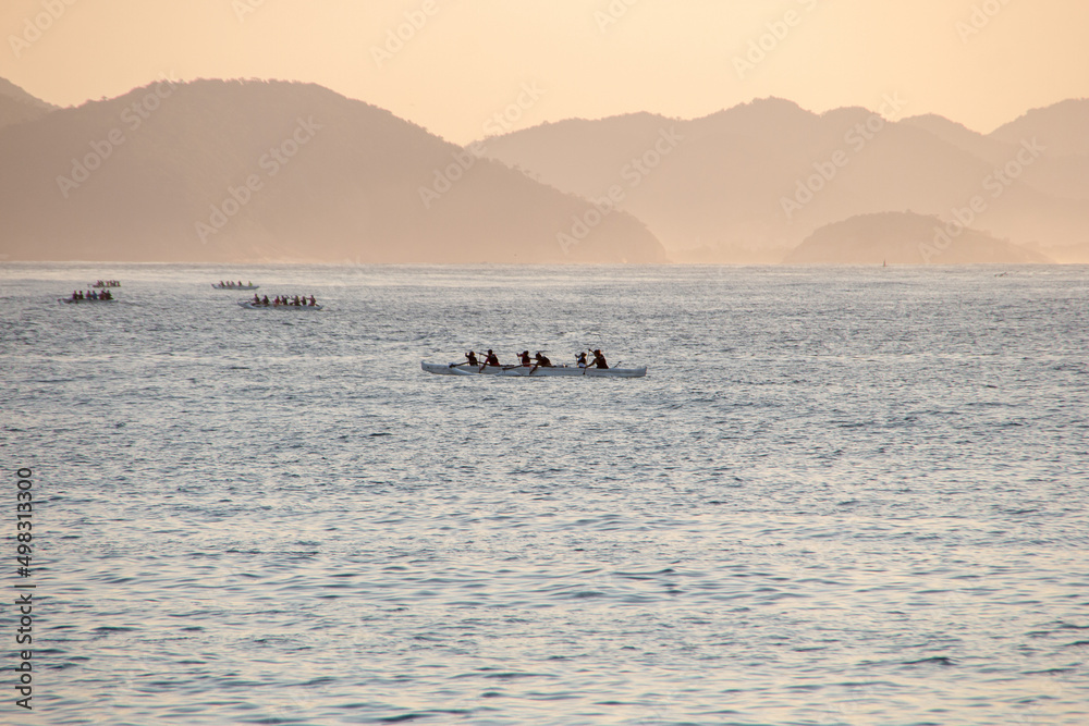 silhouette of people paddling a hawaiian canoe at Copacabana Beach in Rio de Janeiro.