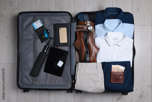 Folded clothes, shoes and accessories in open suitcase on wooden background, top view. Packing for business trip photo