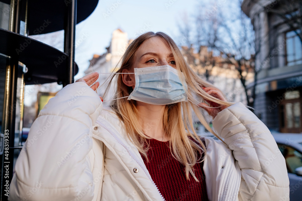 A beautiful girl puts on and takes off a medical mask. Protection from coronavirus on the street in a pandemic. High quality photo A beautiful girl puts on and takes off a medical mask. Protection from coronavirus on the street in a pandemic. High quality photo