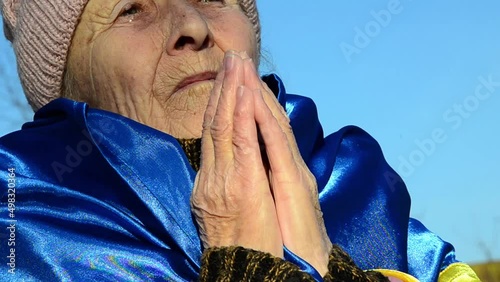 A woman in prayer for peace in Ukraine. The old grandmother is wrapped in the flag of Ukraine. Ukrainian refugees. A woman prays for an end to the war. Russian aggression against Ukraine. War in Ukrai photo