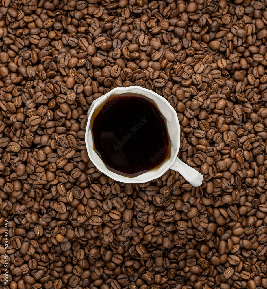 A white cup of black coffee in a mountain of coffee beans A white cup of black coffee in a mountain of coffee beans