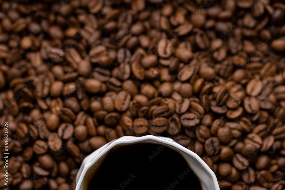 A partially visible white cup of black coffee surrounded by coffee beans A partially visible white cup of black coffee surrounded by coffee beans