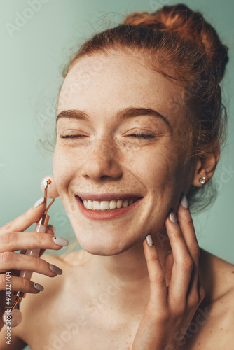 Close-up portrait of a freckled woman massaging face by jade roller massager, enjoying skincare rejuvenating procedure. Facial skincare. Natural beauty. Facial photo
