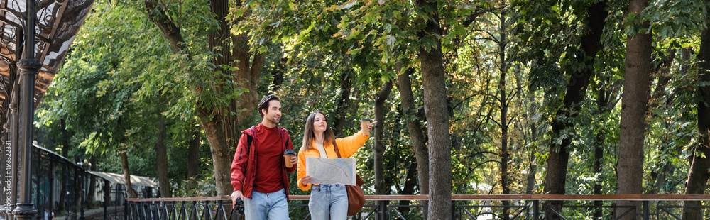 Traveler holding takeaway drink and binoculars near girlfriend with map on urban street, banner. Traveler holding takeaway drink and binoculars near girlfriend with map on urban street, banner.