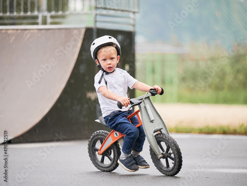 Child riding balance bike. Male toddler kid in helmet learning to ride on run bicycle at skate park. © anatoliy_gleb