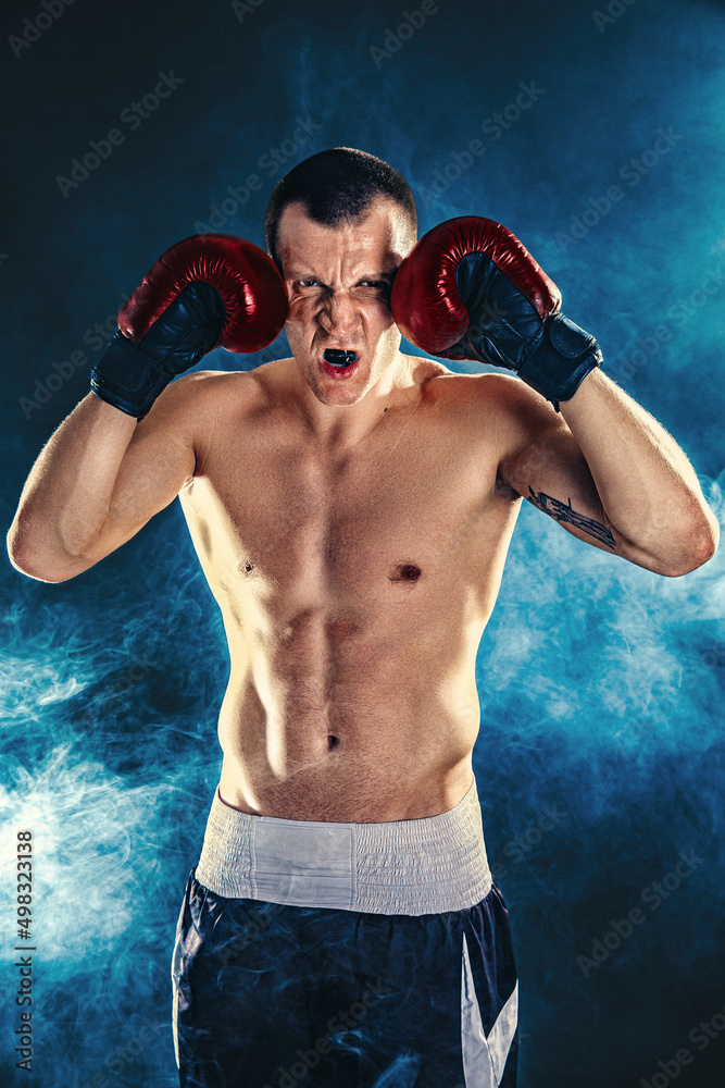 Winner of competitions. Studio portrait of a muscular boxer in professional gloves of European appearance with light bristles and hair on his chest. Smoke in background 