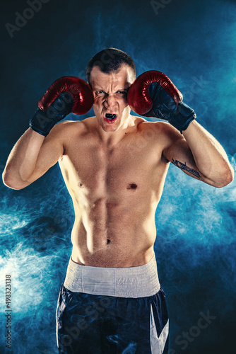 Winner of competitions. Studio portrait of a muscular boxer in professional gloves of European appearance with light bristles and hair on his chest. Smoke in background  © zamuruev
