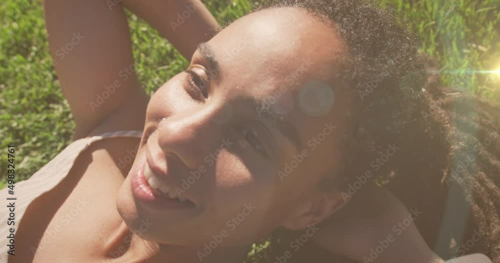 Animation of light spots over smiling biracial woman lying in park Animation of light spots over smiling biracial woman lying in park