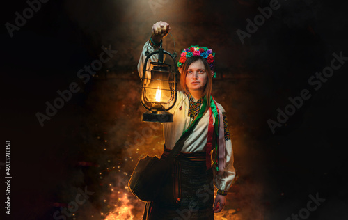 Girl in traditional, national clothes, Ukrainian woman. In hands holds an old gas lamp. Illuminates a narrow passage in the dark basement, bomb shelter. Ukraine. Copy space. War concept