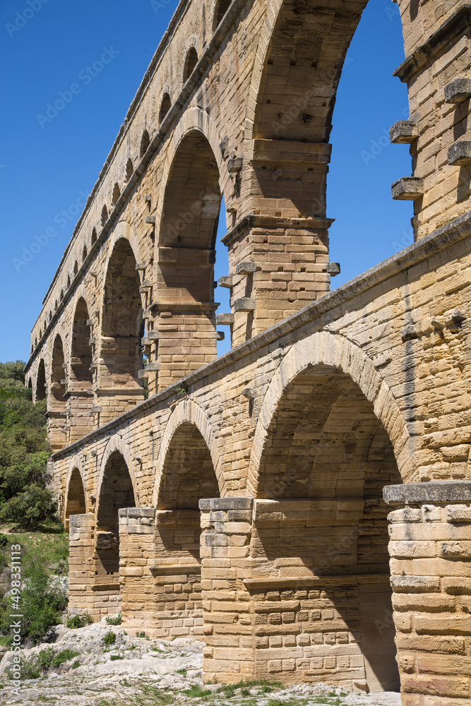 Lateral view of the famous Pont du Gard- iconic ancient Roman bridge, aqueduct and engineering masterpiece in Provence, France. It is formed by three floors of arcades, massive arches and pillars.