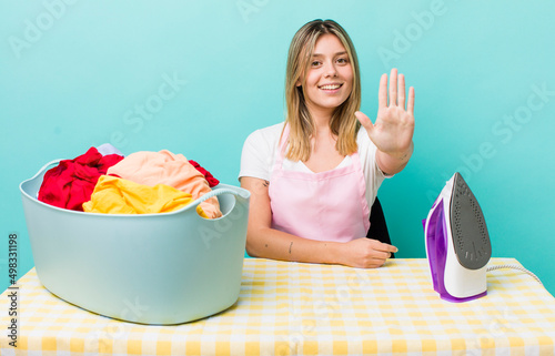 pretty blonde woman smiling and looking friendly, showing number five. iron and clothes concept photo