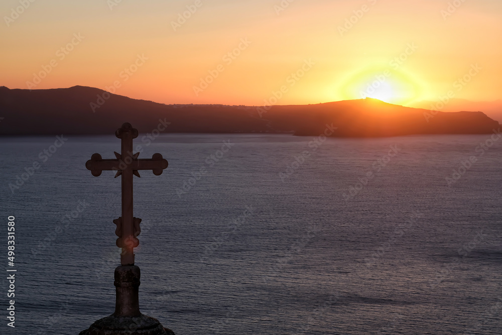 A religious cross of a Greek orthodox church and a dramatic sunset in Fira Santorini