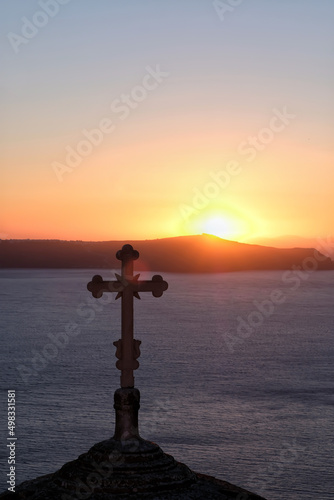 View of a religious Orthodox Church and a cross on the top while the sun is setting in a spectacular way